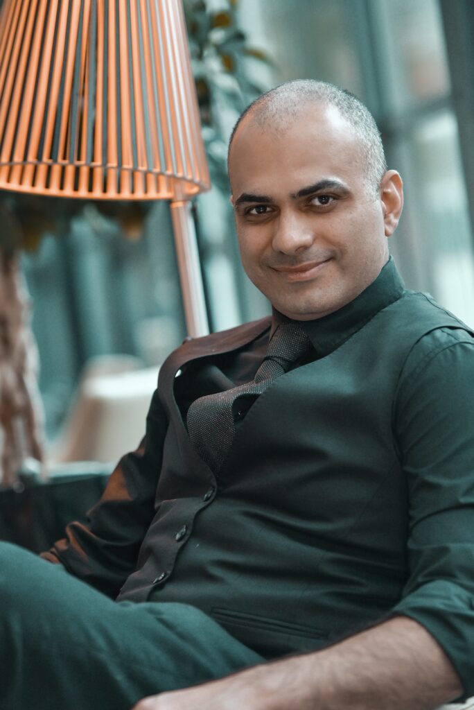 Man in black vest and tie smiles towards camera.